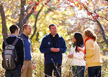 A Jesuit priest chats with students on campus                    